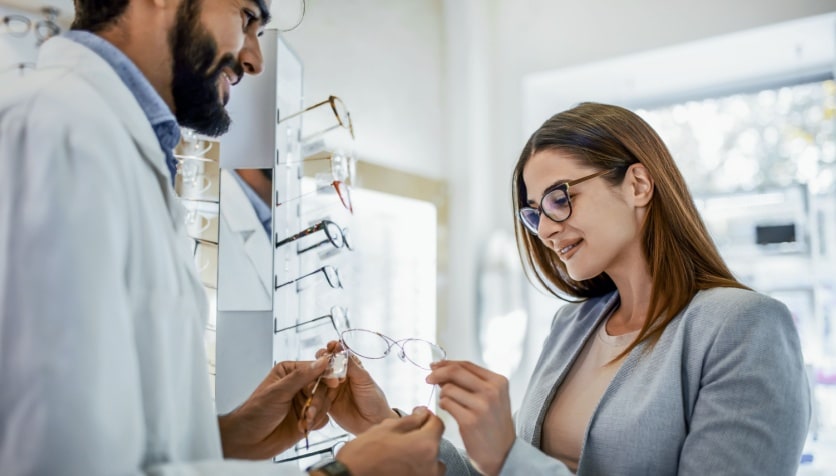 A woman with myopia wearing glasses at her optician's office wearing glasses looking at a new pair of frames.