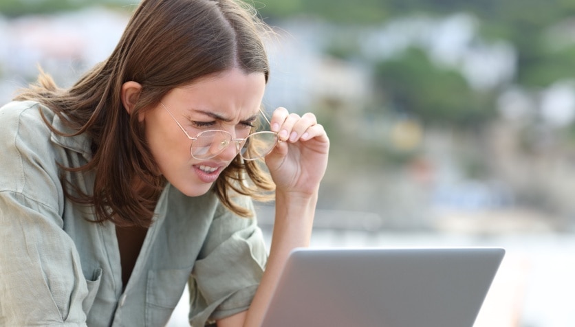 A woman with presbyopia squinting as she adjusts her glasses to look at her computer.