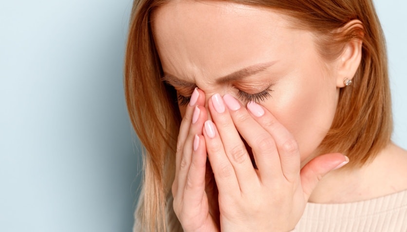 A woman with her eyes closed and hands placed on her face as she looks for a lost contact lens.