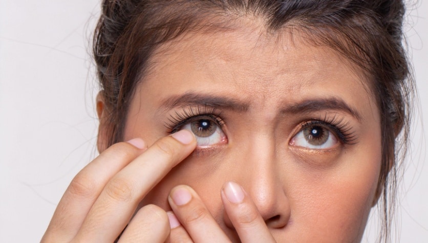 A woman with one finger near her eye as she struggles to remove a stuck contact lens.