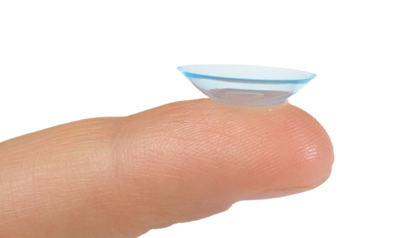 An image of an inside out contact lens, with the edges flipped out, balanced on a fingertip.