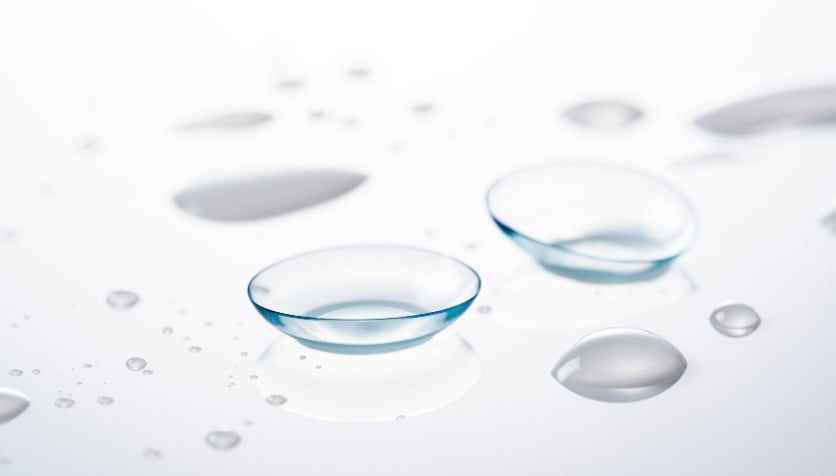 Image of two contact lenses on a glass tabletop with contact lens solution droplets.