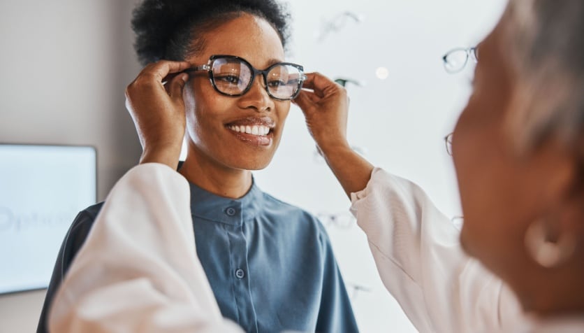 A woman getting fitted for eyeglasses at her optician's office, with special attention to frame temple size.