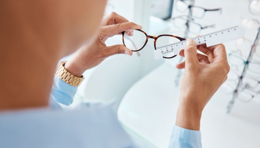 An optician measuring the frame size of a pair of glasses with a ruler at the eye doctor.