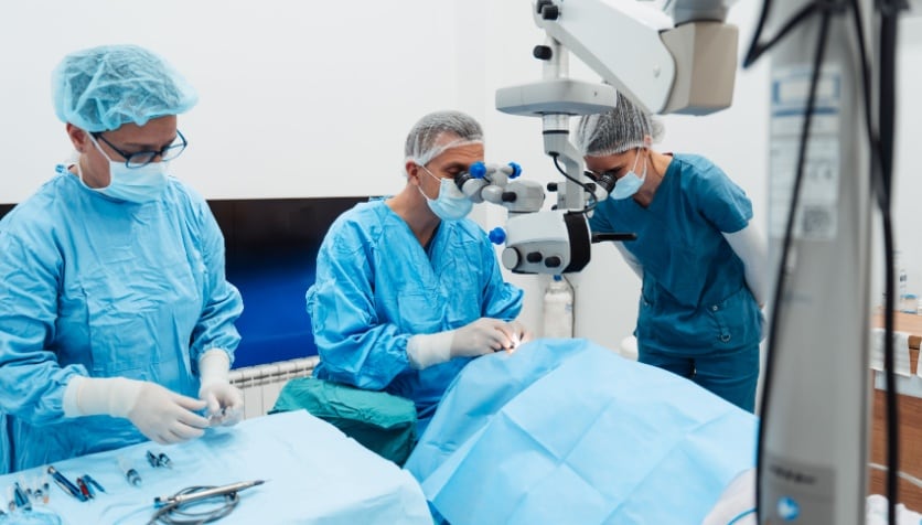 Two eye care professionals and one eye surgeon performing cataract surgery on a patient.