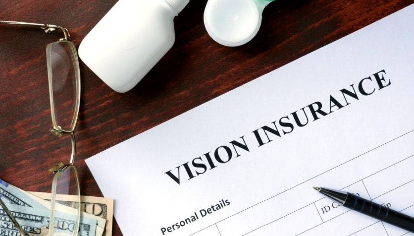 Eyeglasses sitting on a desk next a pen and paperwork labeled as "Vision Insurance."