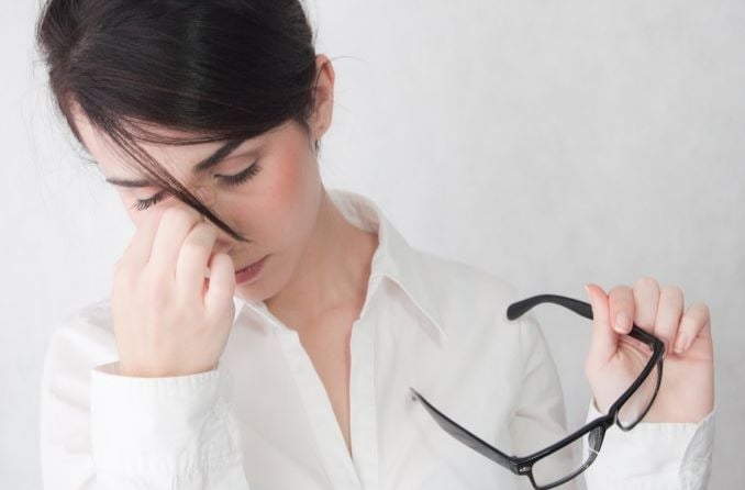 Woman with eye strain holding glasses