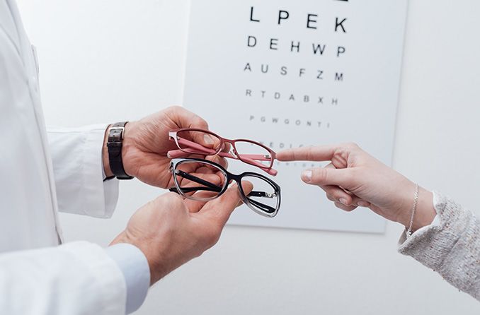 Eye chart in background with person choosing pair of eyeglasses from an optometrist