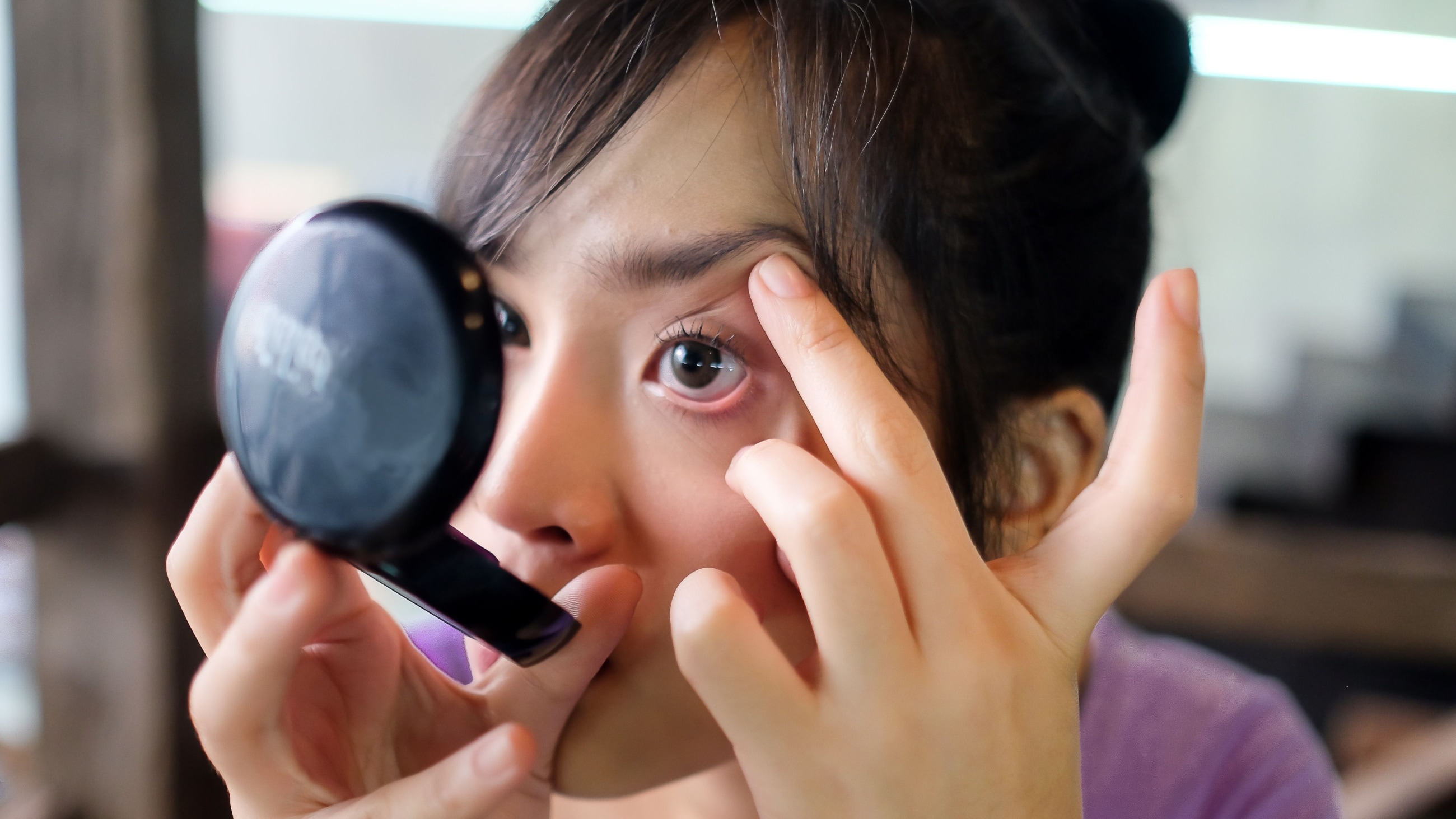 woman looking at a compact mirror trying to get something out of her eye