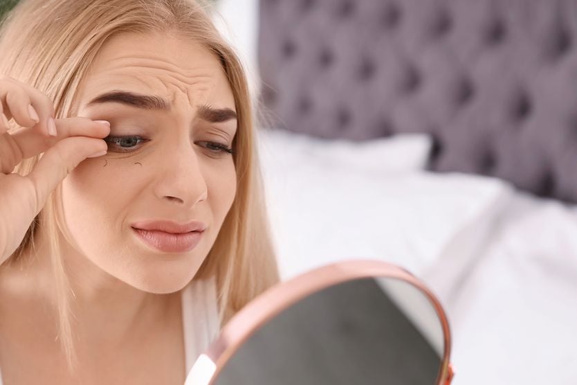 worried woman pulling out her eyelashes looking in a mirror