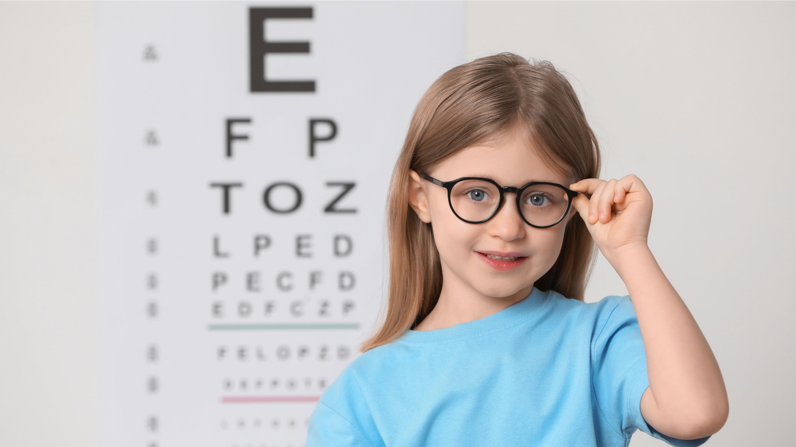 Young girl wearing glasses for myopia standing in front of a Snellen eye chart. Young girl wearing glasses for myopia standing in front of a Snellen eye chart.