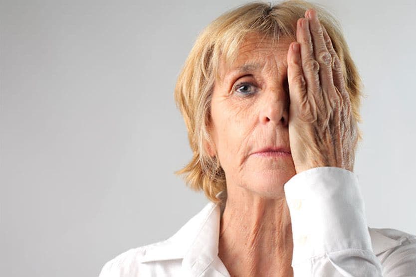 woman with one hand over her eye taking a visual acuity test for cataracts