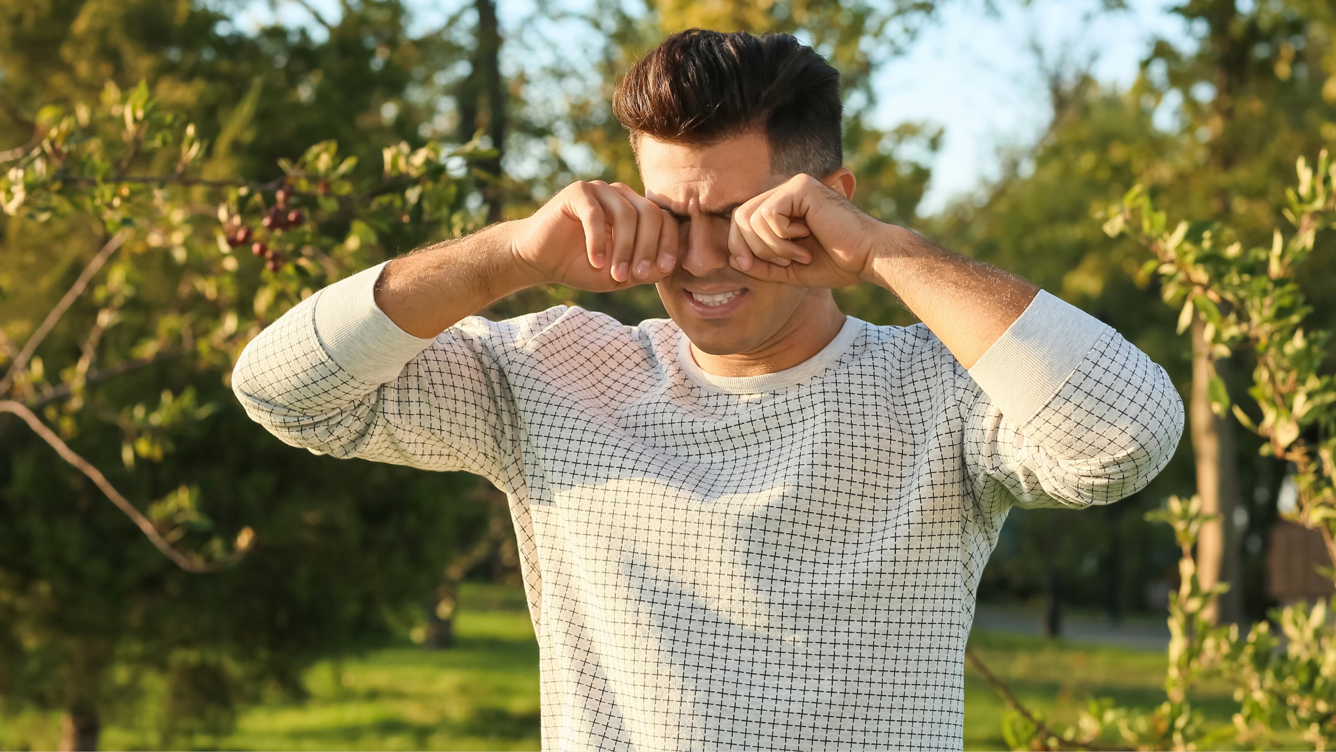 man rubbing eyes with allergies sitting on a park bench man rubbing eyes with allergies sitting on a park bench