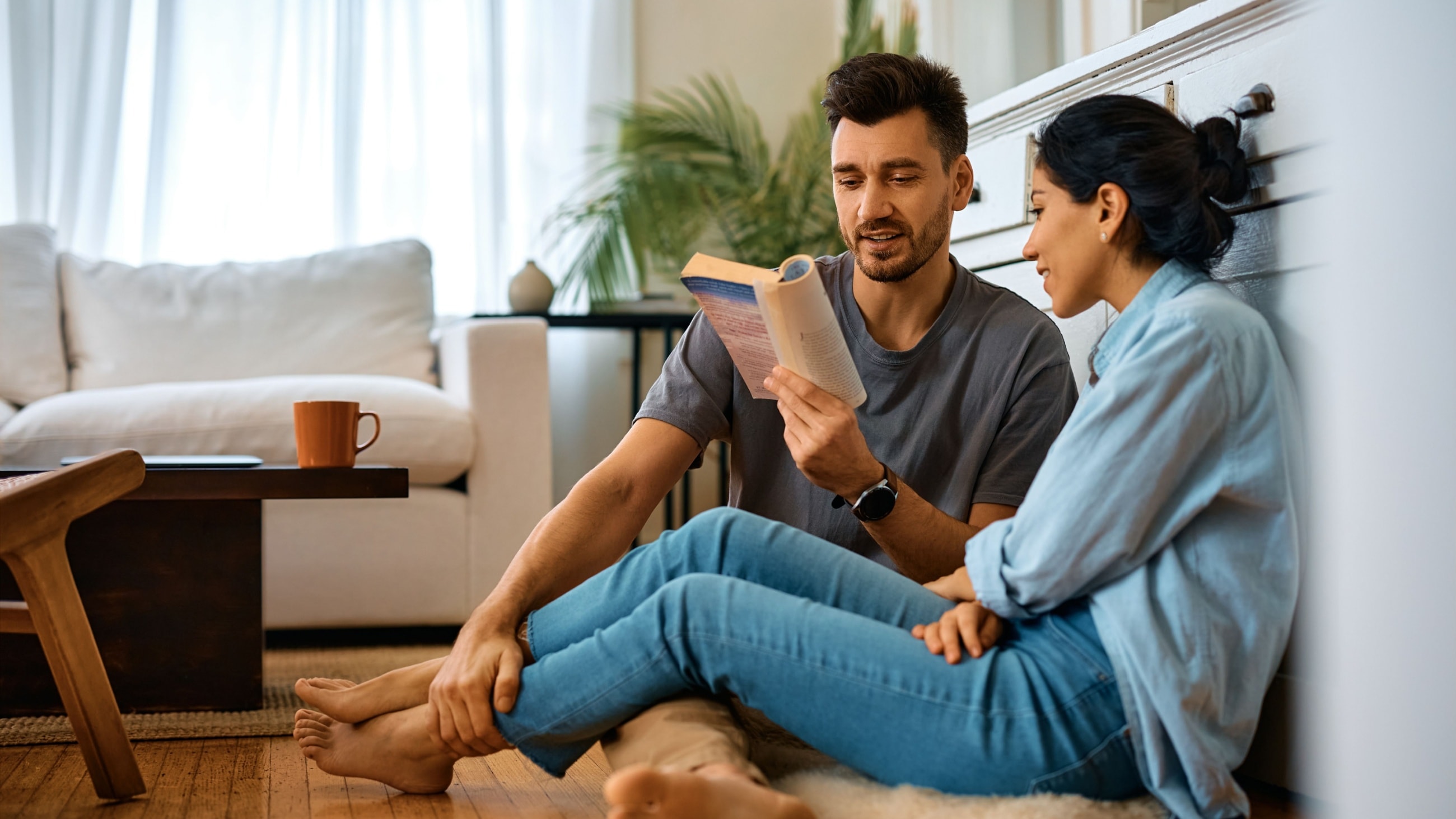 Smiling man reading book to his wife while spending time together at home.