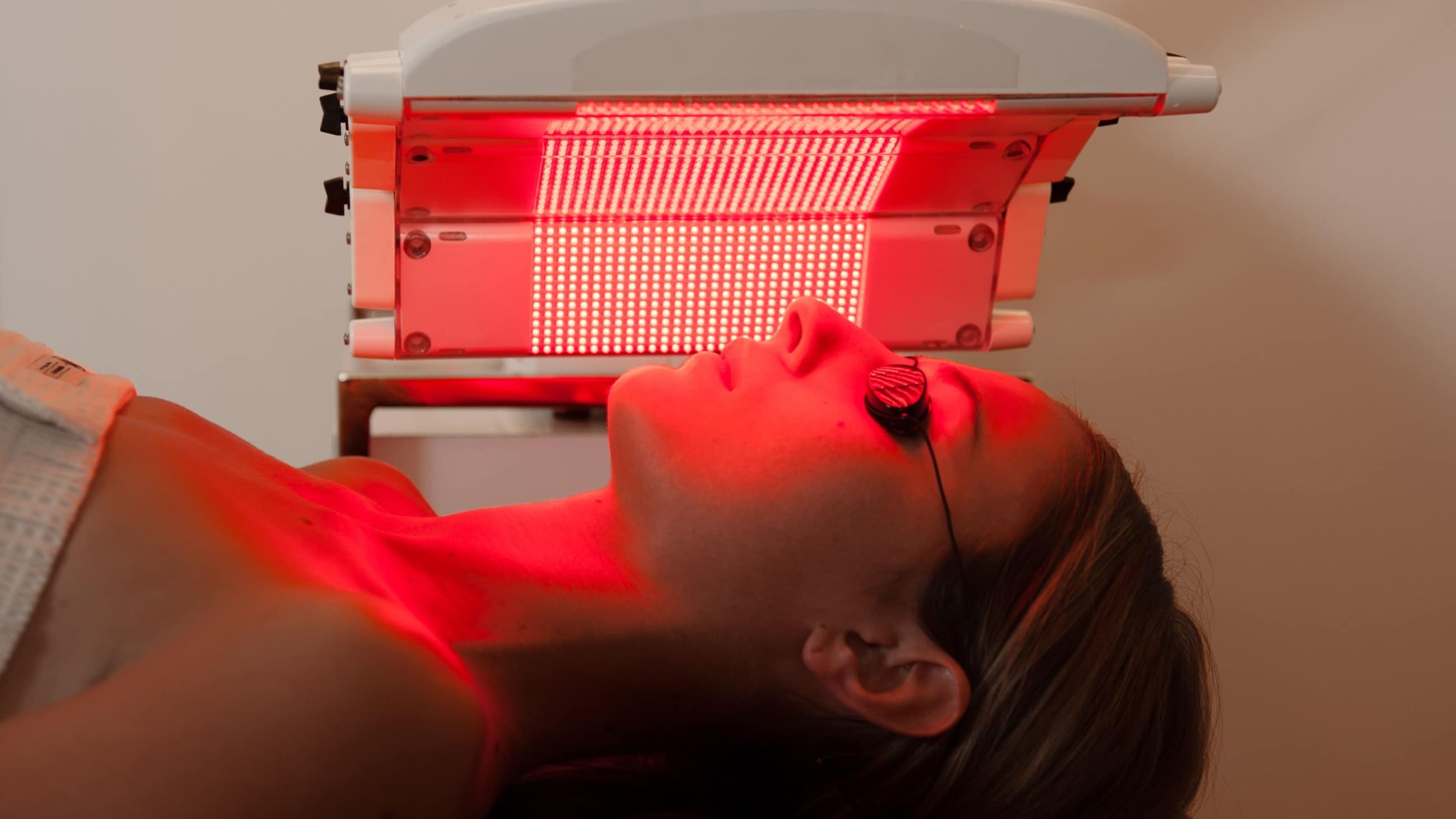 woman under a red light lamp (undergoing red light therapy)