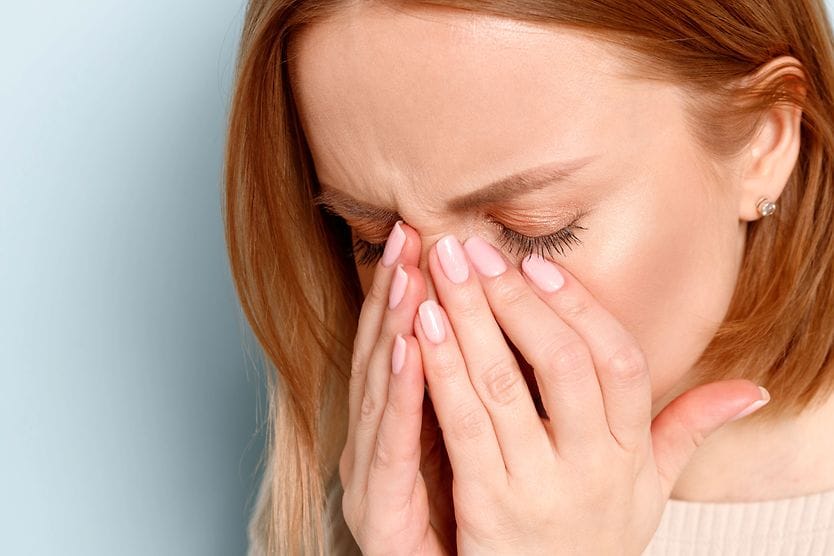 A woman with her eyes closed and hands placed on her face as she looks for a lost contact lens.