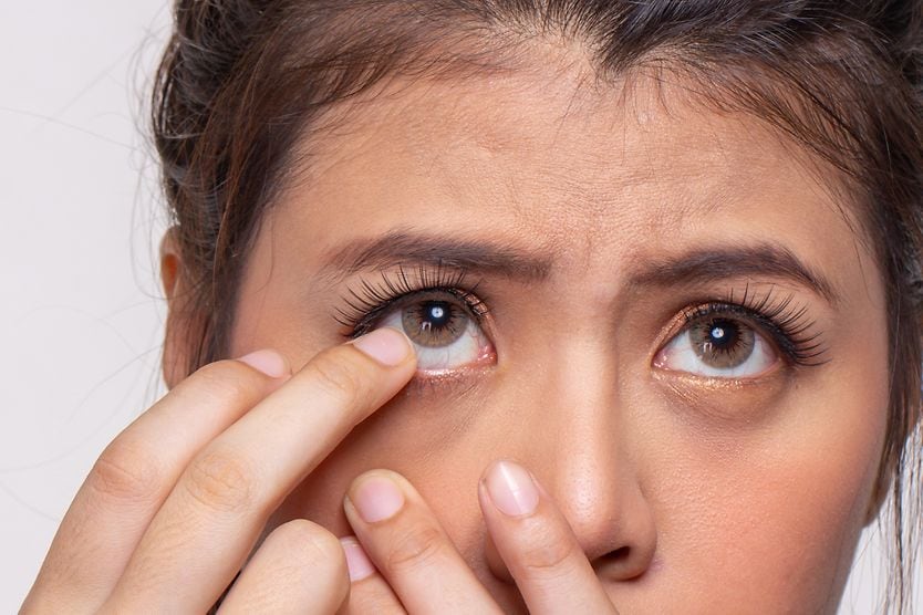 A woman with one finger near her eye as she struggles to remove a stuck contact lens.