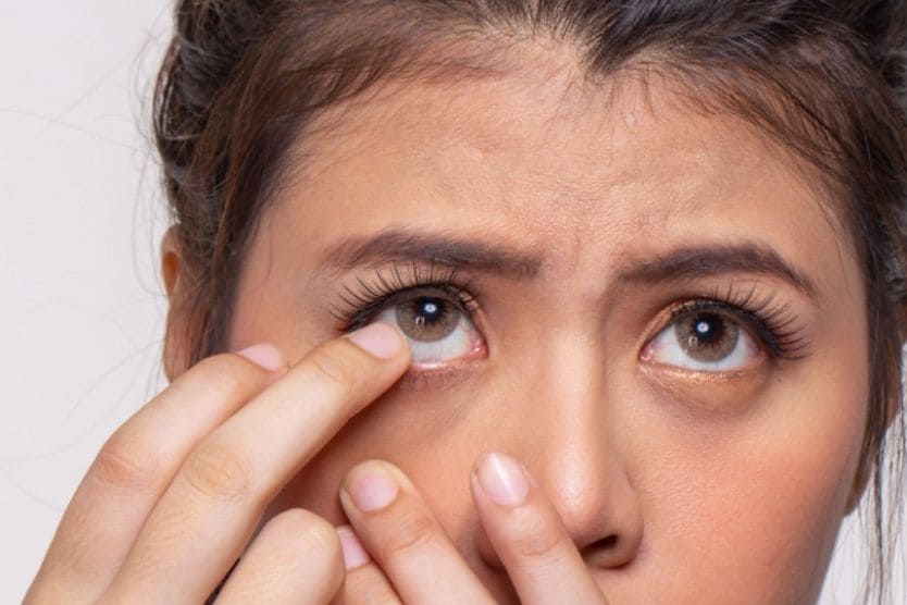 A woman with one finger near her eye as she struggles to remove a stuck contact lens.
