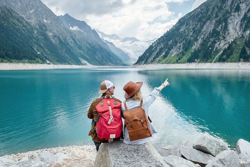 People sitting on rock, looking out at lake and mountains.