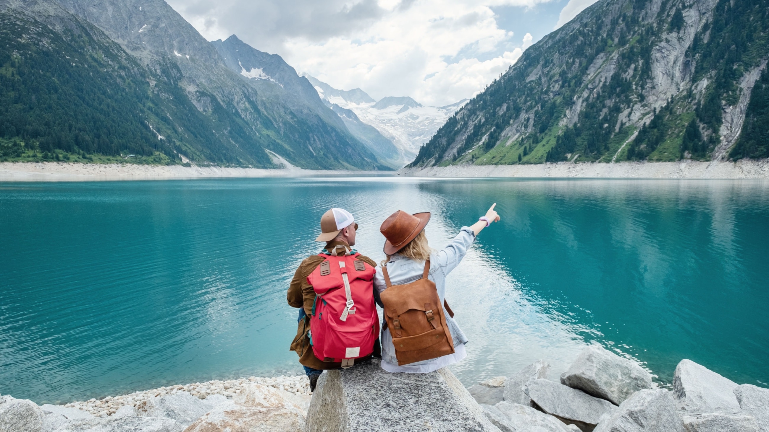 People sitting on rock, looking out at lake and mountains.