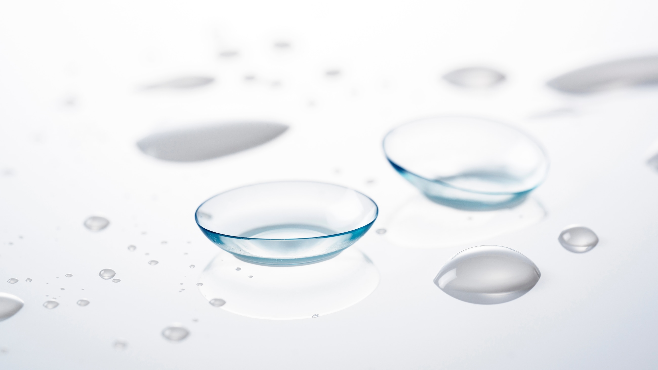 Image of two contact lenses on a glass tabletop with contact lens solution droplets. Image of two contact lenses on a glass tabletop with contact lens solution droplets.