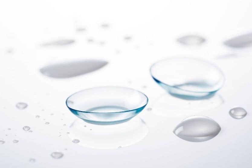 Image of two contact lenses on a glass tabletop with contact lens solution droplets. Image of two contact lenses on a glass tabletop with contact lens solution droplets.