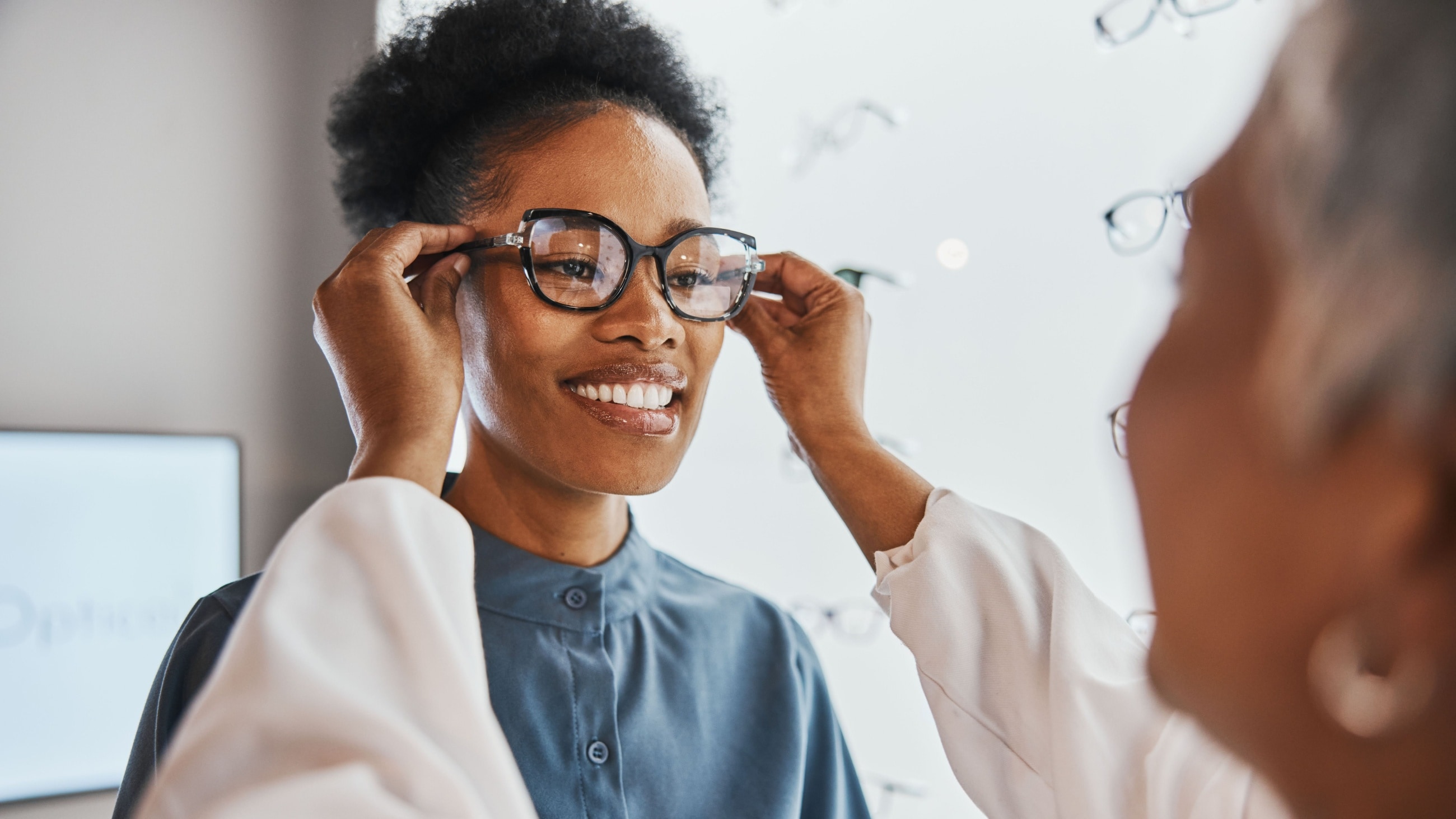 A woman getting fitted for eyeglasses at her optician's office, with special attention to frame temple size.
