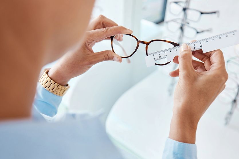 An optician measuring the frame size of a pair of glasses with a ruler at the eye doctor.