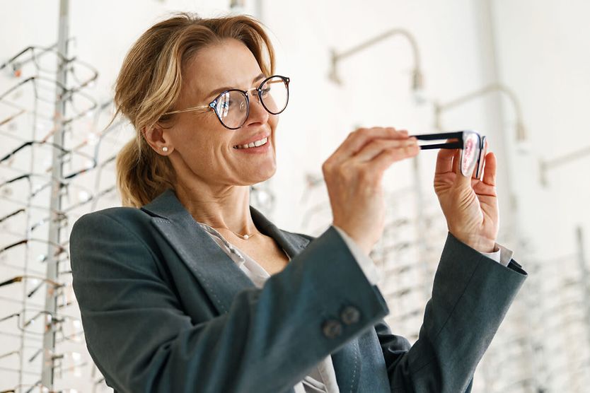 Woman chooses between two glasses in an optician's shop.