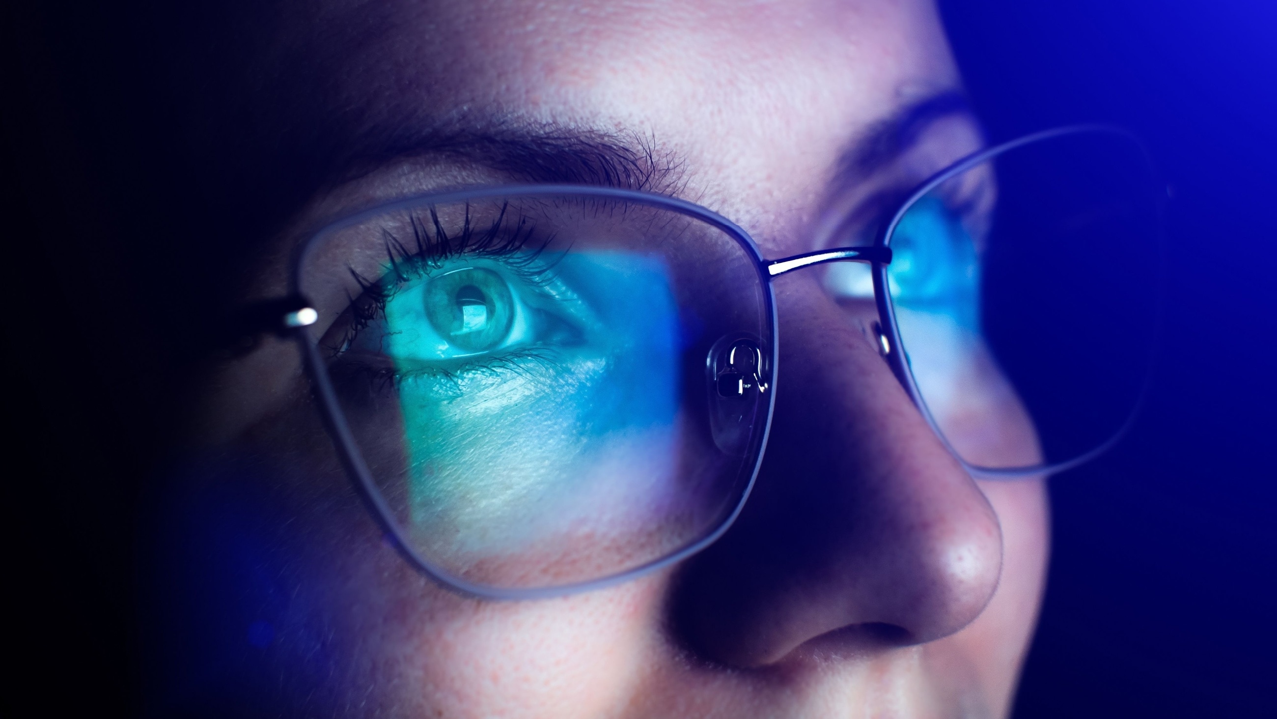 man wearing eyeglasses with computer screen in reflection of eyeglass lenses