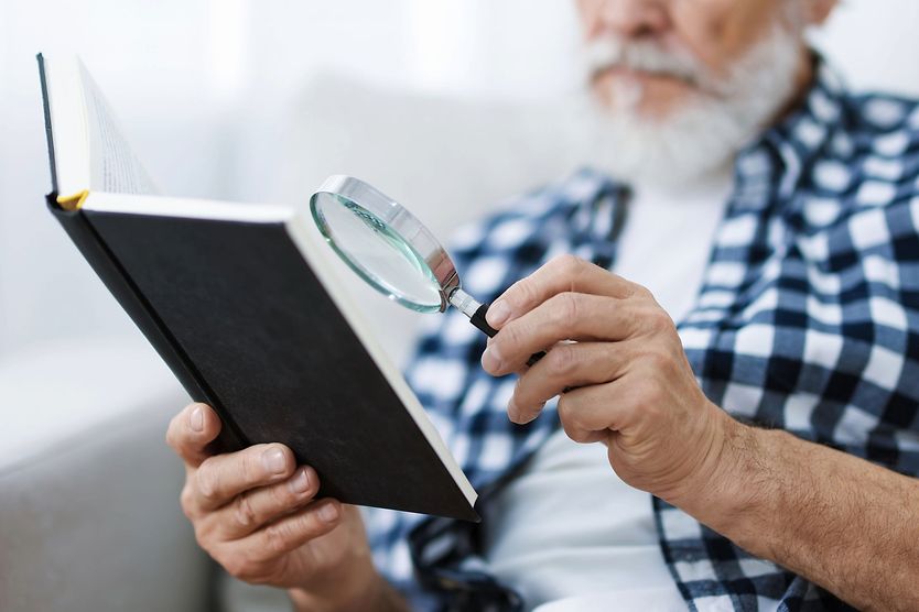 elderly man using low vision magnifier to read a book elderly man using low vision magnifier to read a book
