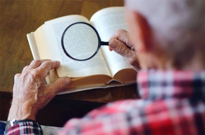 elderly man using low vision magnifier to read a book