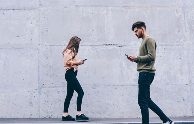 young man and woman looking at their cell phones young man and woman looking at their cell phones