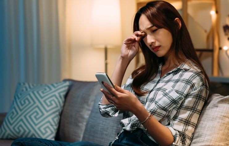 Young woman with eye pain looking at smartphone Young woman with eye pain looking at smartphone