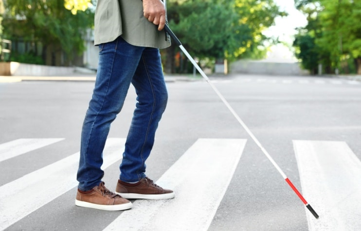 Person with low vision using white cane crossing street