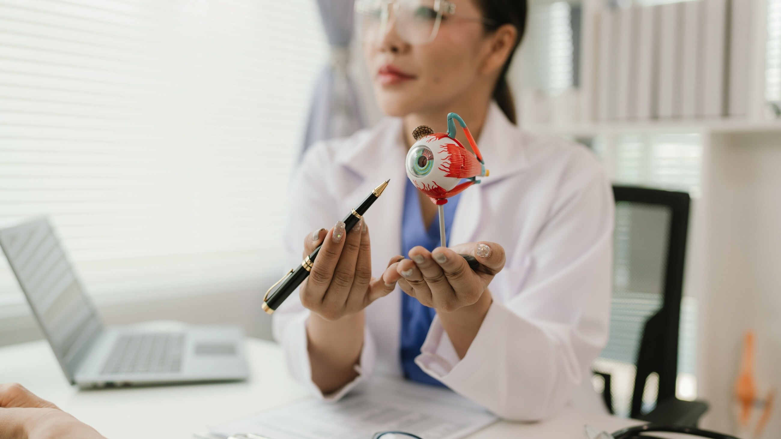 Close-up of Asian female doctor talking with elderly patient showing eyeball model.