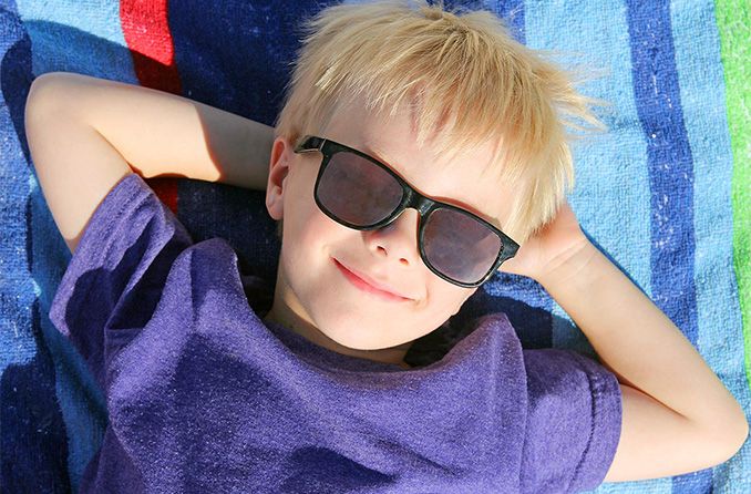 boy laying on beach towel wearing sunglasses boy laying on beach towel wearing sunglasses
