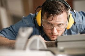 man wearing safety goggles and headphones while working with a saw