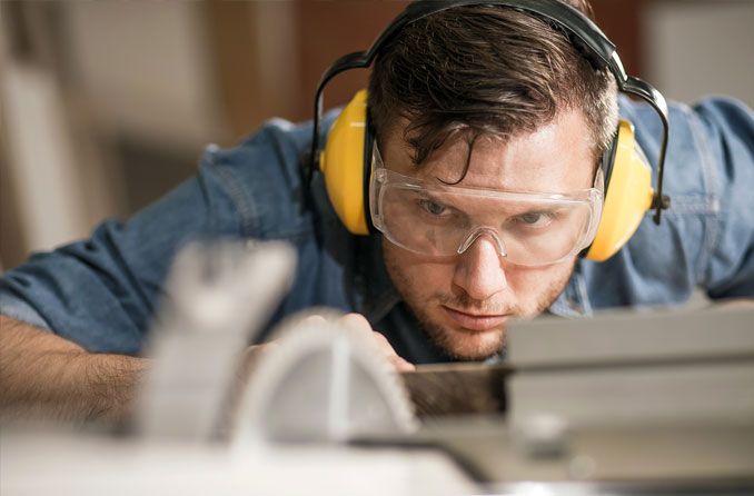 man wearing safety goggles and headphones while working with a saw man wearing safety goggles and headphones while working with a saw