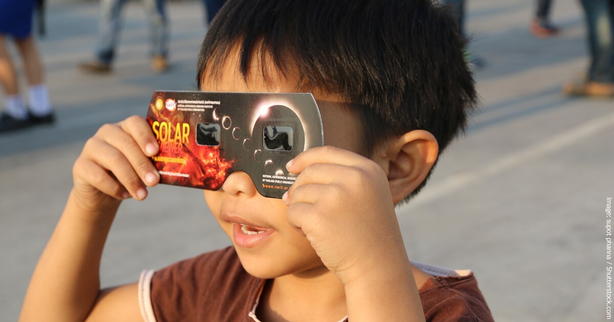 Little boy looking through eclipse glasses looking up at the solar eclipse.
