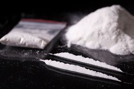 Plastic packet, two lines and pile of cocaine on black background, closeup.