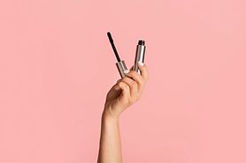 person's hand holding hypoallergenic mascara on pink background