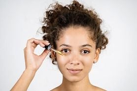 Young woman applying eye serum with a serum dropper.