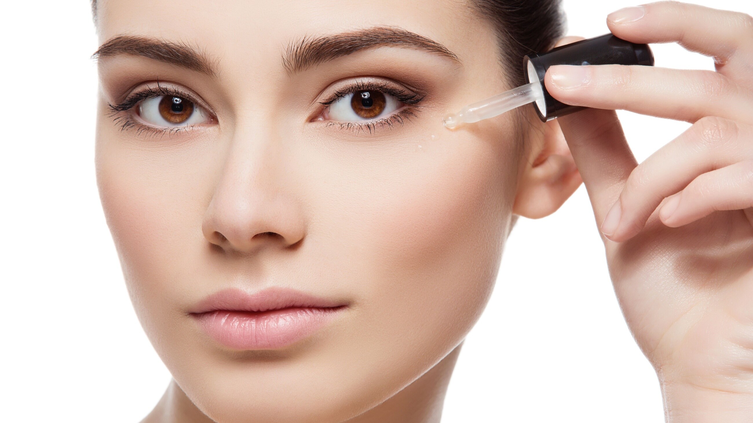 Young woman applying eye serum with a serum dropper.