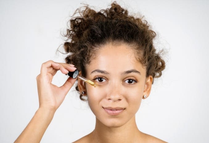 Young woman applying eye serum with a serum dropper. Young woman applying eye serum with a serum dropper.