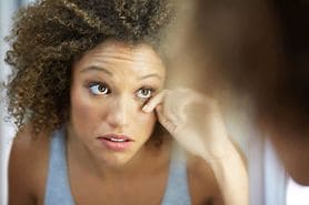 woman looking in the mirror with fake eyelashes and an eye infection