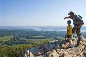 father pointing to horizon with son on top of a mountain