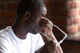 Young man with asthenopia (eye strain) holds his glasses and rubs his eyes.