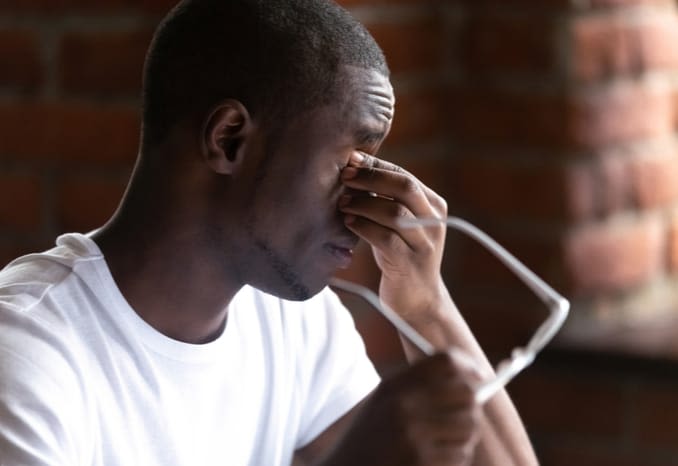 Young man with asthenopia (eye strain) holds his glasses and rubs his eyes. Young man with asthenopia (eye strain) holds his glasses and rubs his eyes.