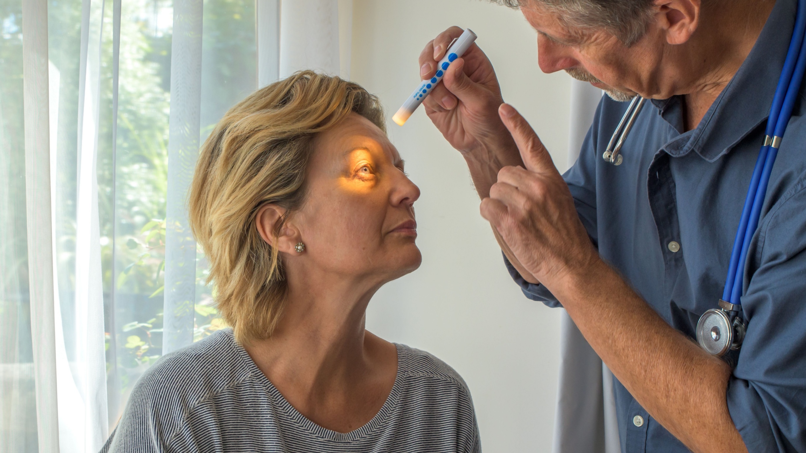 Eye doctor checking woman's eyes with light